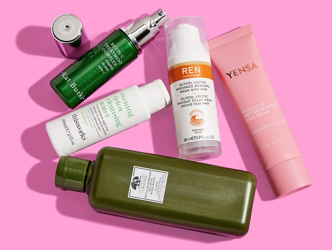 Skincare products from various brands scattered on pink background