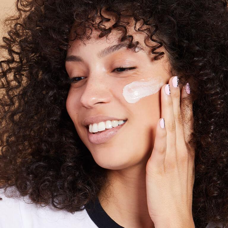 An image of a smiling model with curly hair applying cream on her cheek and an image of DERMA E Vitamin C Concentrated Serum