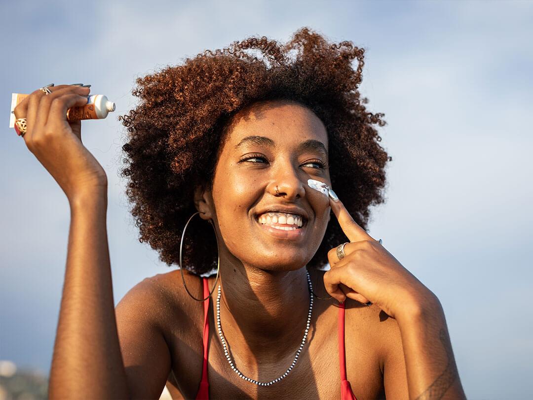 Woman with natural curly hair applies sunscreen to her face
