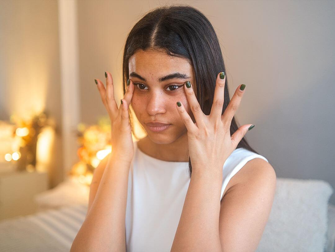 A young woman gently applying castor oil under her eyes with her fingers to treat dark circles